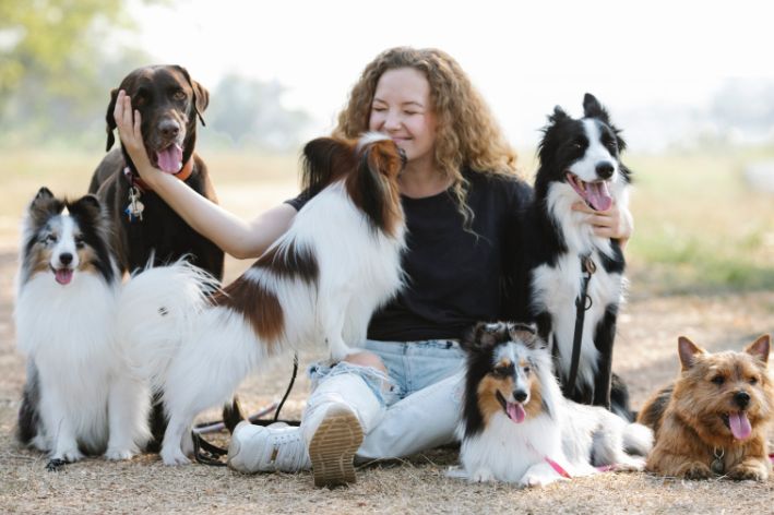 mulher passeando com vários cachorros em um parque e um deles lambendo o seu rosto